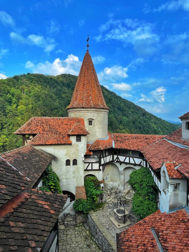 Explore the iconic Bran Castle, nestled in the scenic hills of Transylvania, Romania, under a vibrant blue sky.